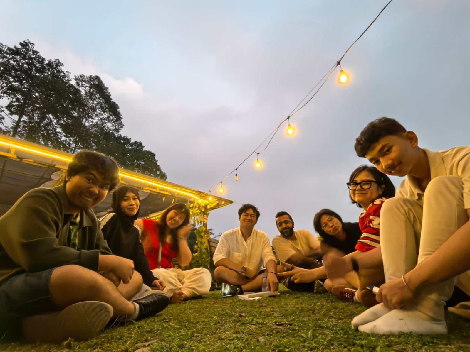 Sitting in a circle on the grass, string lights on